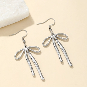 Silver liquid metal bow earrings with mirrored surface on a minimalist stone background