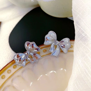Boucles d'oreilles nœud argenté avec texture métallique sur plateau en céramique