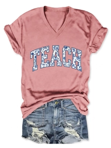 Dettaglio delle lettere TEACH con motivi floreali blu su una maglietta rosa con scollo a V