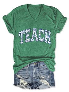 Dettaglio flat lay della maglietta con scollo a V, stampa TEACH floreale e shorts