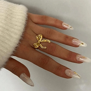 Detail of 18K gold plated stainless steel bow ring worn on a finger with white nails