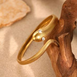 Golden snake-shaped bangle with scale texture and crystals on a natural wood display