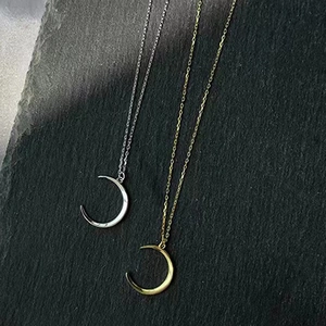 Minimalistische Mondhalsketten in Gold und Silber auf einem dunklen Steinhintergrund