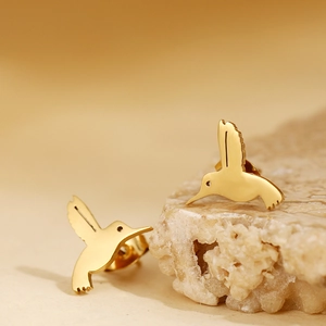 Minimalist golden hummingbird stud earrings displayed on natural stone with warm background