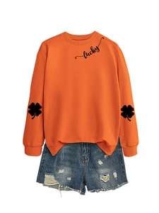 Detail of lucky text and clover prints on an orange sweatshirt with denim shorts