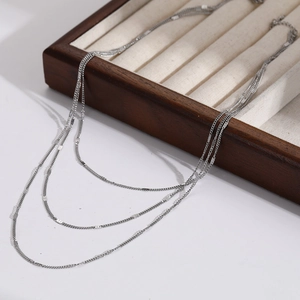 Collier argenté à trois couches avec paillettes sur plateau, style minimaliste chic