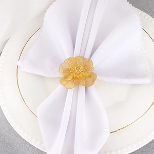 Golden hollow floral napkin ring with mesh texture on a white napkin and dinner plate