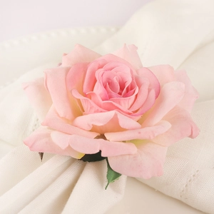 Pink fabric rose napkin ring with green leaves on white textured dinner plate