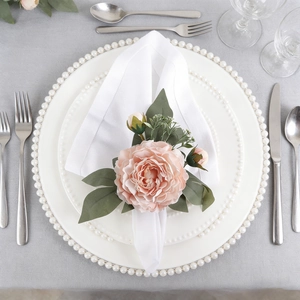 Servilletero artesanal de rosa rosa claro con hojas sobre elegante plato blanco de cena