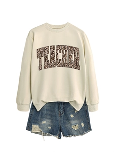 Detail of white teacher sweatshirt with leopard print text and distressed denim shorts