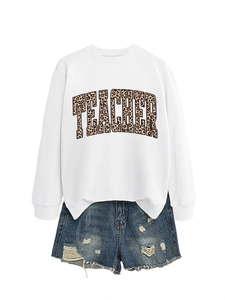 Close-up of white crewneck sweatshirt with leopard print TEACHER text and ripped denim shorts