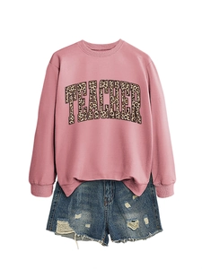 Flat lay of pink crewneck teacher sweatshirt with leopard print text and denim shorts