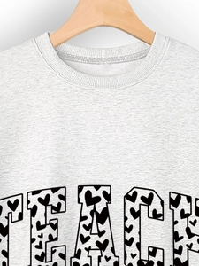 Close-up of grey sweatshirt featuring TEACH text print with black heart pattern details