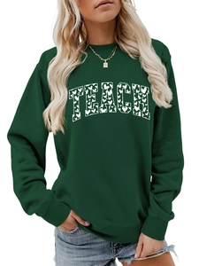 Close-up of white TEACH text with heart patterns on dark green crewneck sweatshirt