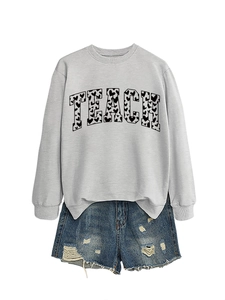 Detail of grey crewneck sweatshirt featuring TEACH lettering with heart patterns and denim shorts