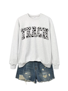 Detail of grey Teach sweatshirt with black heart-filled letters and denim shorts
