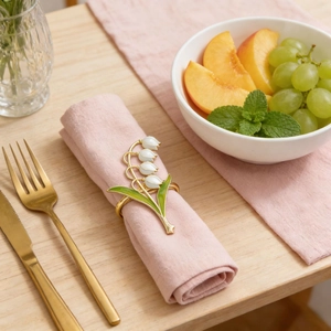 Golden lily of the valley napkin ring with white enamel flowers on a pink napkin