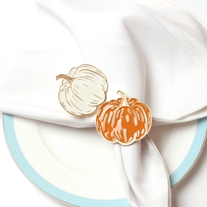 Detail of white and orange enamel pumpkin napkin rings with gold metal trim on a plate