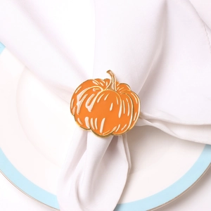 Close-up of orange enamel pumpkin napkin ring with gold metallic edges on white linen