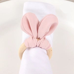 Pink fabric bunny ear napkin ring with natural wooden loop on white linen napkin