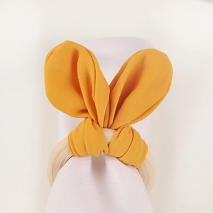 Detail of a bright yellow rabbit ear fabric napkin ring with a natural wooden base