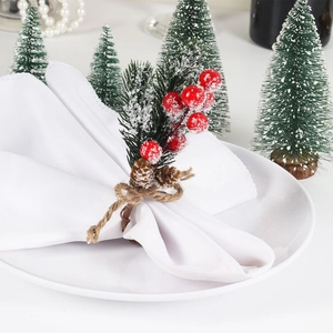 Christmas napkin ring with cedar needles, red berries and pine cones on white plate