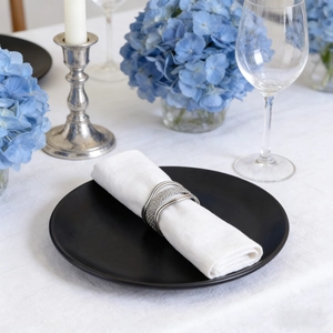 Silver woven layered metal napkin ring on white cloth napkin with elegant dinnerware