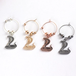 Exaggerated snake-shaped wine glass charms in four metallic finishes on white background