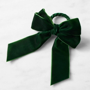 Detalle de servilletero con lazo grande de terciopelo verde oscuro sobre mármol