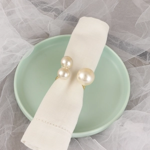 Elegant gold twisted metal napkin ring featuring three cream pearls on a linen napkin