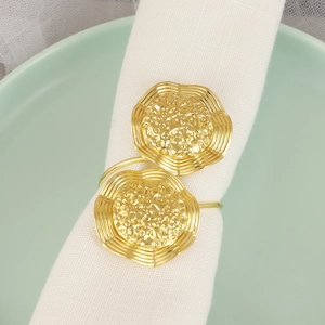 Elegant gold metal flower napkin rings with wavy edges on a white cloth and ceramic plate