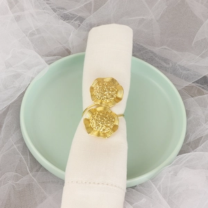 Golden metal flower napkin ring with hammered texture on a white cloth and green plate