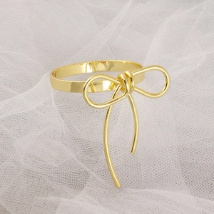 Detailed close-up of a golden metal bow napkin ring on a soft white textured fabric