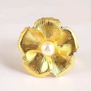 Détail d'un rond de serviette en fleur dorée avec une perle blanche centrale élégante