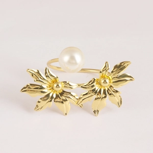 Macro detail of gold-plated leaf napkin ring with large white pearl on pink surface