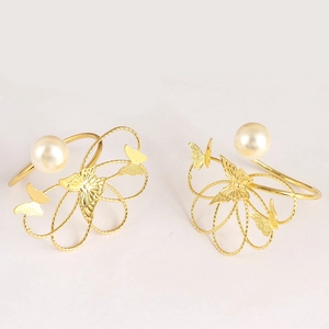 Detalle de servilletero dorado con mariposa, perla blanca y diseño floral calado de lujo