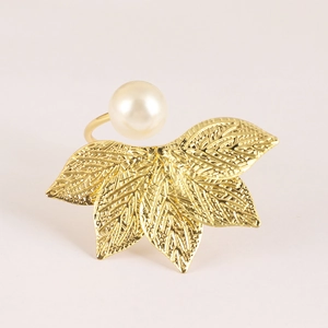 Macro detail of golden metal leaf napkin ring featuring a white pearl and intricate veins