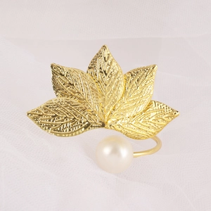 Golden leaf napkin ring with a white pearl accent on a minimalist white mesh background
