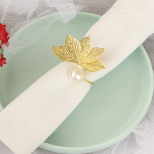 Detail of golden leaf napkin ring with pearl accent on a white folded linen napkin