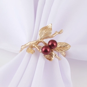 Detail of a golden branch napkin ring with red berries and leaves on white linen