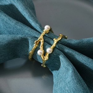 Golden branch-shaped napkin ring with three white pearls on a blue textile napkin