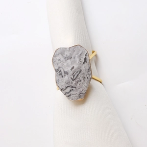 Macro shot of marble stone napkin ring with gold rim detail on white linen fabric