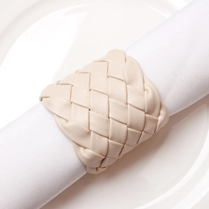 Handwoven beige leather napkin ring on white fabric napkin and ceramic plate
