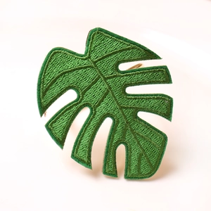 Handmade green monstera leaf embroidered napkin ring with a golden metal circle base