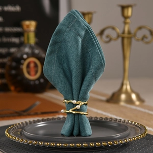 Golden branch-shaped napkin ring with white pearls and a green folded napkin
