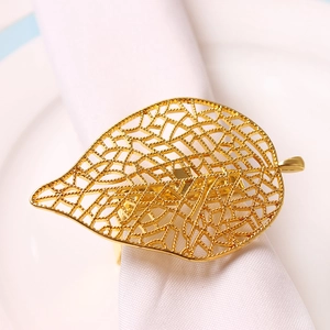 Détail d'un rond de serviette en forme de feuille dorée ajourée sur nappe blanche