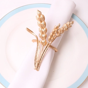 Elegant gold wheat ear napkin ring in polished alloy on a white plate with linen napkin