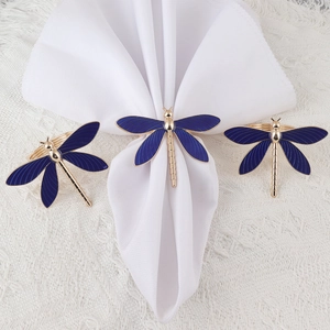 Blue dragonfly napkin rings with gold trim set on white cloth for dining table setup