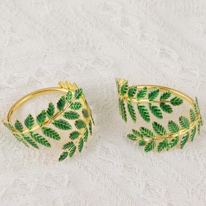 Detail of golden metal napkin ring with green enamel leaf design on lace background