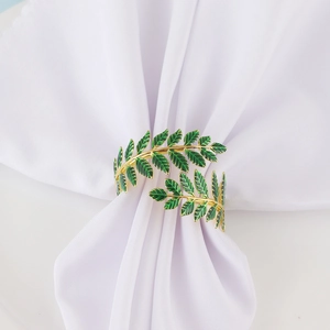 Elegant gold olive leaf napkin ring with green enamel finish on white fabric